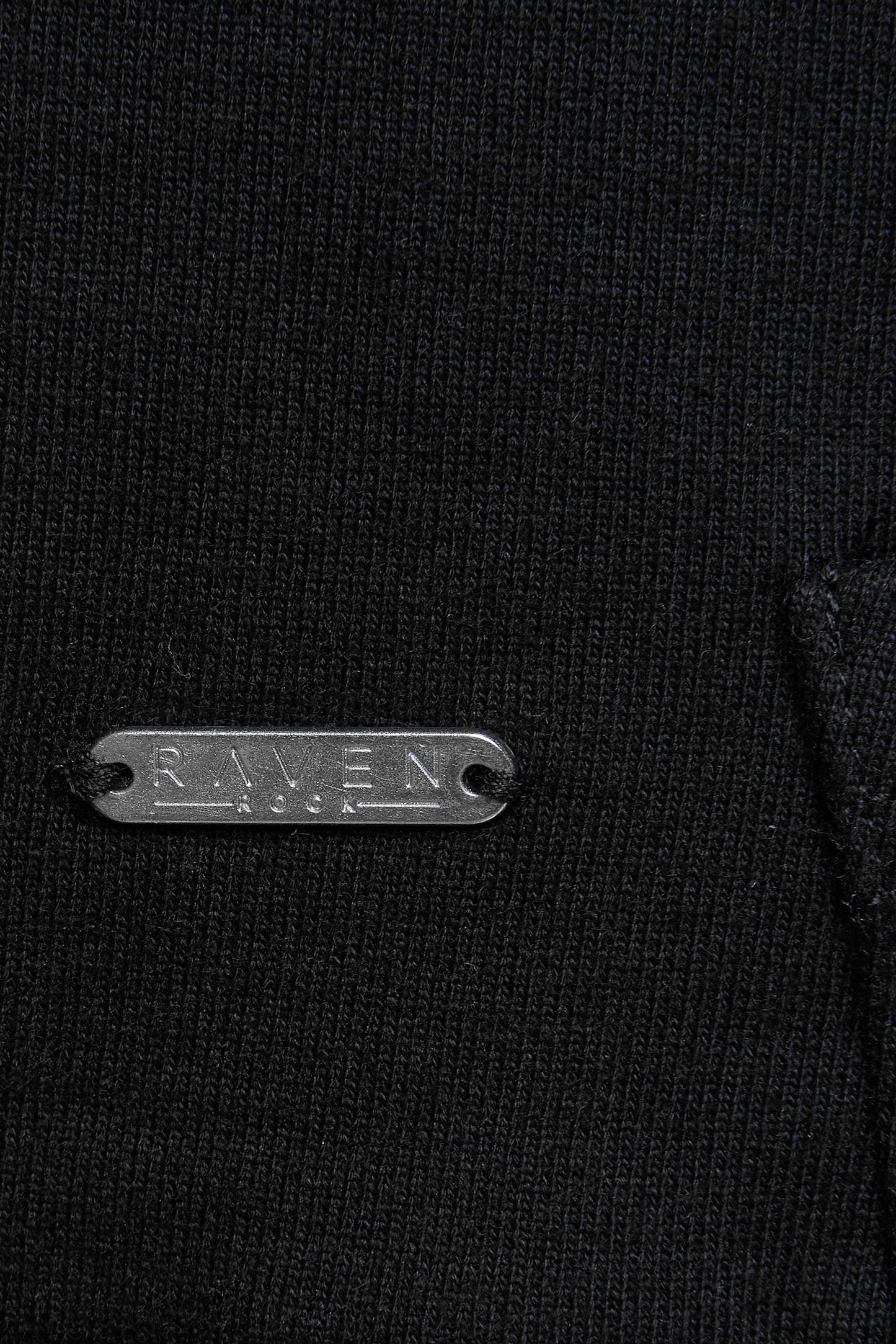 Close-up of a black garment with a branded metal label on a black hoodie