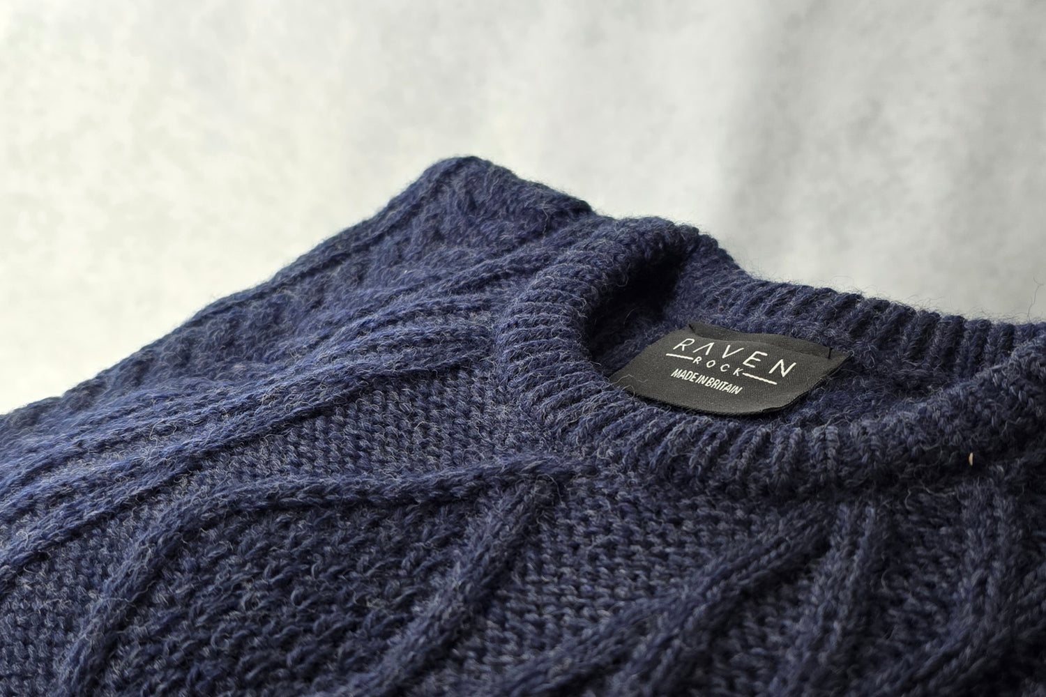 Close-up of a blue knitted sweater with a brand label on a light gray background